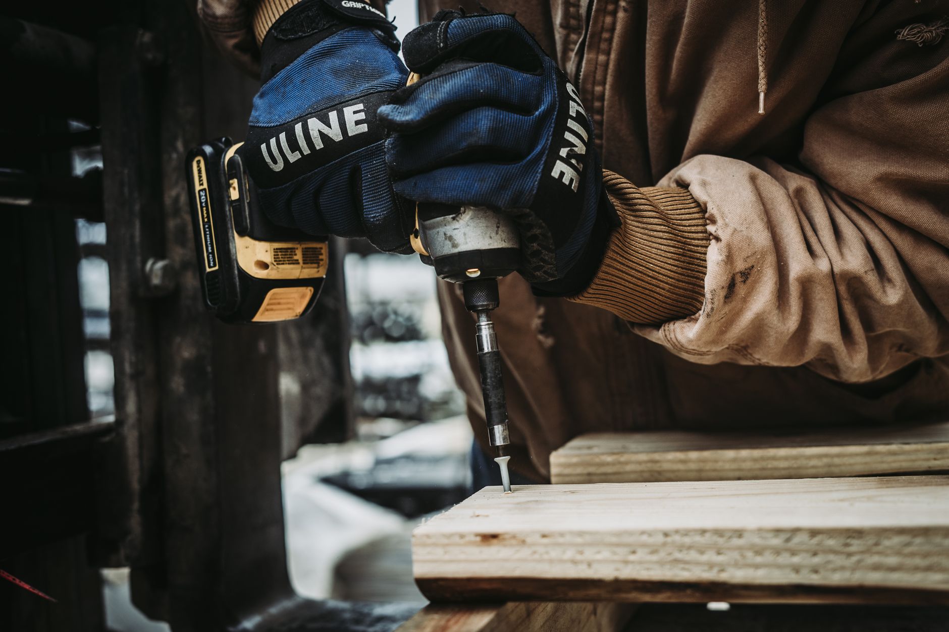 Artisan portant des gants de protection et utilisant une perceuse-visseuse sur une planche de bois