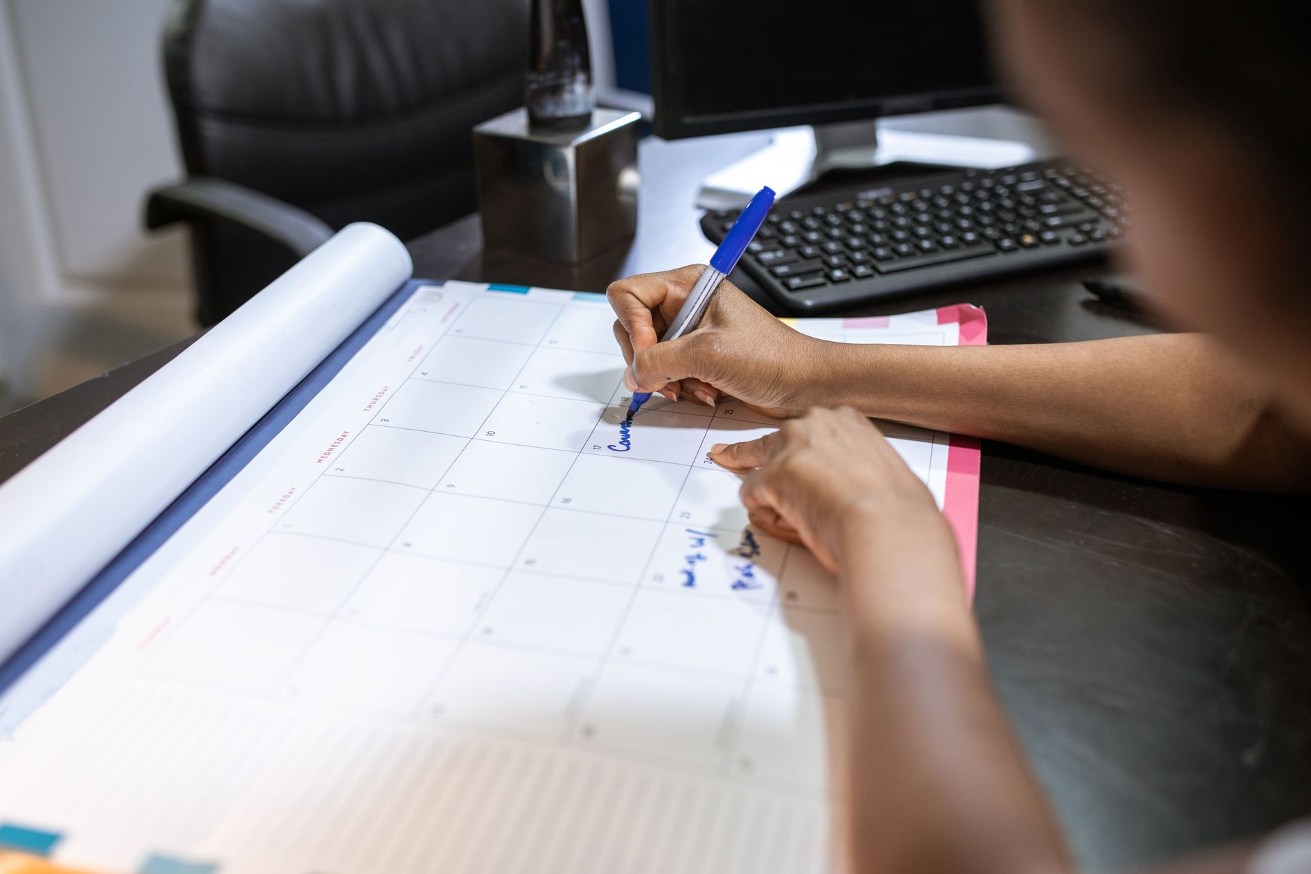 Gros plan sur une personne qui remplit un calendrier de planning posé sur un bureau professionnel