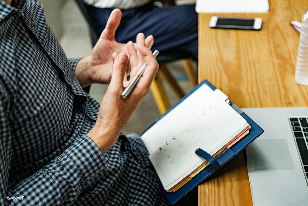 Personne planifiant des dates dans un agenda papier au bureau, ordinateur portable à proximité